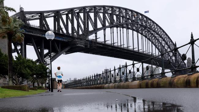 SYDNEY, AUSTRALIA - NewsWire Photos OCTOBER 6, 2022: A person walks in the rain with the Sydney Harbour bridge pictured in the background.Picture: NCA NewsWire / Damian Shaw