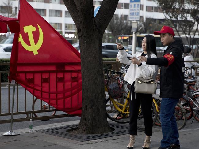 In this Oct. 16, 2017 photo, a deputized citizen gives direction to a resident near a Chinese Community Party flag on the streets of Beijing, China. Extraordinary security measures are being imposed ahead of the party congress, in addition to the typical security forces, thousands of deputized citizens patrol the streets, and knife, fireworks and chemical sales have been suspended. (AP Photo/Ng Han Guan)