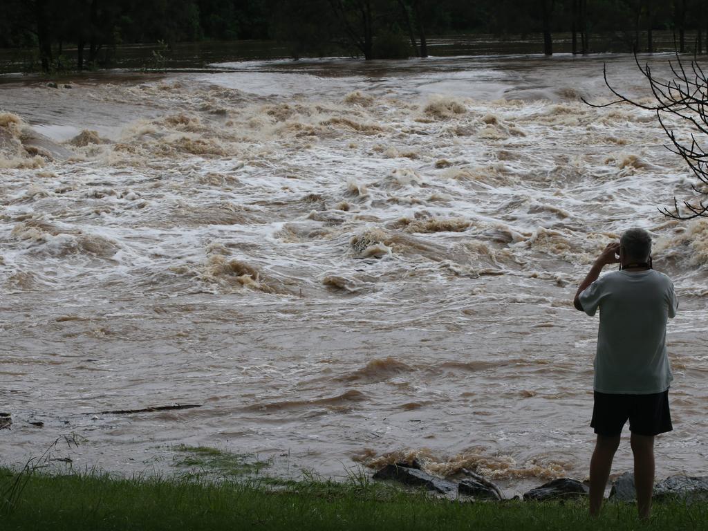 People gather to watch floodwaters in the Coomera River spill over the Oxenford Weir. Picture Glenn Hampson