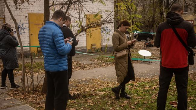 Residents in Kherson, Ukraine, use their phones in an area of the city centre that has temporary phone network and a Starlink device last November. Picture: Getty Images