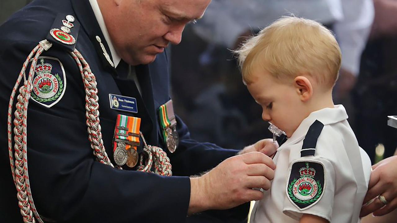 The heartbreaking image of RFS Commissioner Shane Fitzsimmons pinning a medal on Harvey Keaton after his father Geoffrey Keaton was posthumously awarded the Commissioner’s Commendation for Extraordinary Service and a Commendation for Bravery. Picture: AFP Photo/New South Wales Rural Fire Service