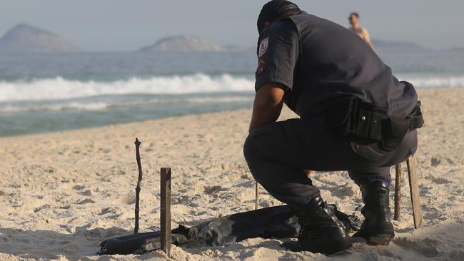 A police officer kneels over a body part, covered in a plastic bag, which was discovered on Copacabana Beach near the Olympic beach volleyball venue.