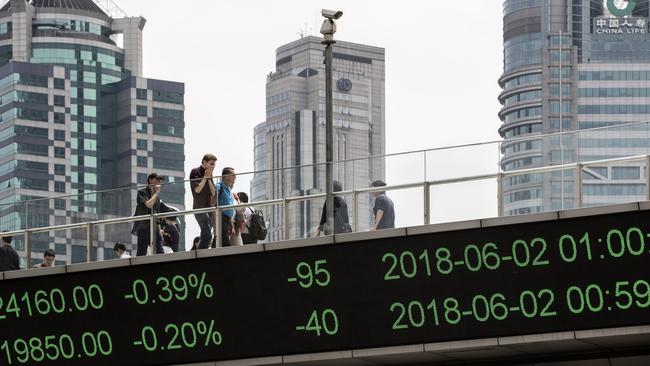 People walk along an elevated walkway as an electronic ticker displays stock figures in Pudong's Lujiazui Financial District in Shanghai, China. Picture: Bloomberg