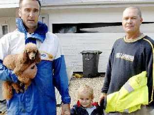 HELPING HAND: Jamie Young (above left) with his son Huey, aged three, and their dog Raja, outside their storm-damaged Lennox Head home with family friend Robbie Clarke. In the background is the wheelie bin blown through the Young family’s garage door.