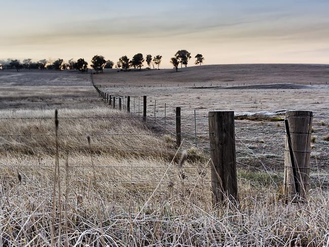 Agricultural farm in Australian Southern Highlands during winter season with frost on wires of paddock fense at sunrise.