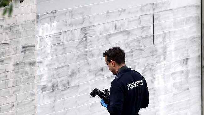 A forensics police officer takes photographs of the wall where anti-Israel graffiti has been removed in Woollahra on Wednesday. The two suspects also torched a car. Picture: David Gray/AFP