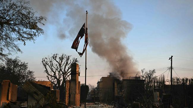 Smoke rises from a destroyed home behind a partially charred US flag during the Palisades fire in Pacific Palisades. Picture: Patrick T. Fallon / AFP