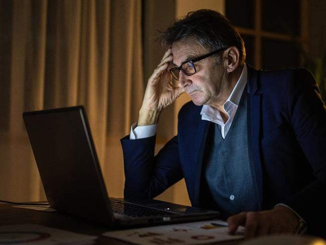 Exhausted mature businessman sitting at the desk, using laptop during night work in office