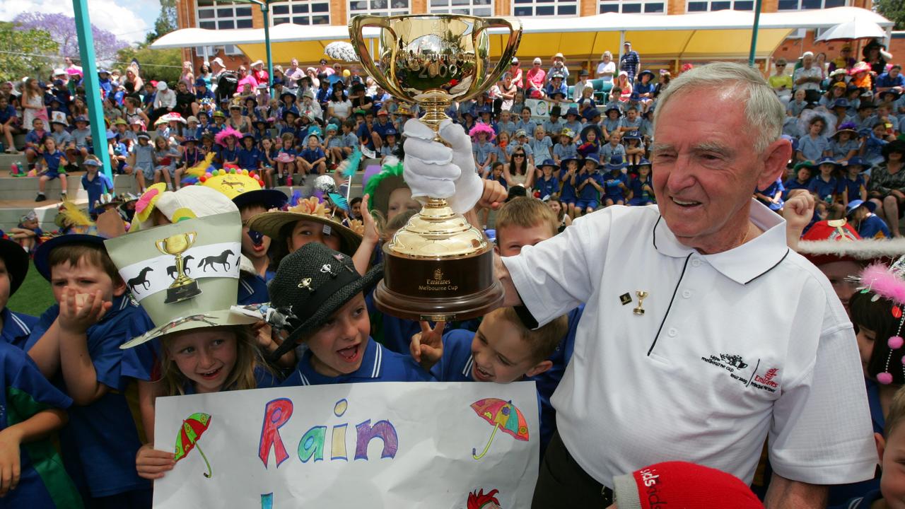 Melbourne Cup at St. Kevin's Primary School Geebung - Three-time winning jockey Jim Johnson 80yrs holding the Melbourne Cup trophy with year one students holding banner with name of racehorse Rain Lover on it.