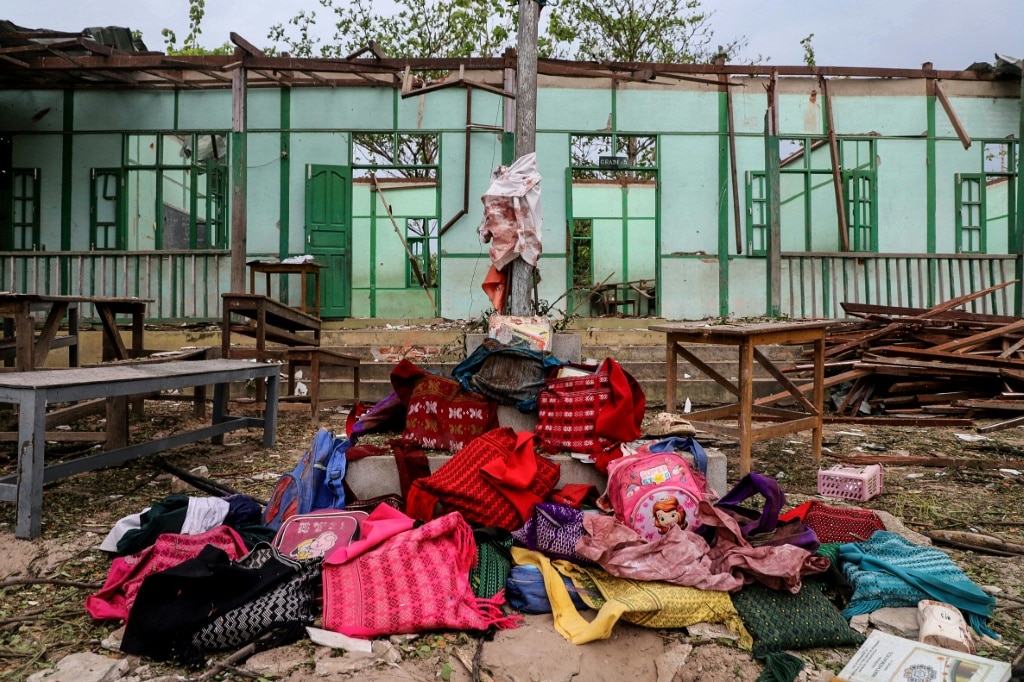 Over a dozen abandoned book bags were piled before a pole flying the Myanmar flag outside the school building