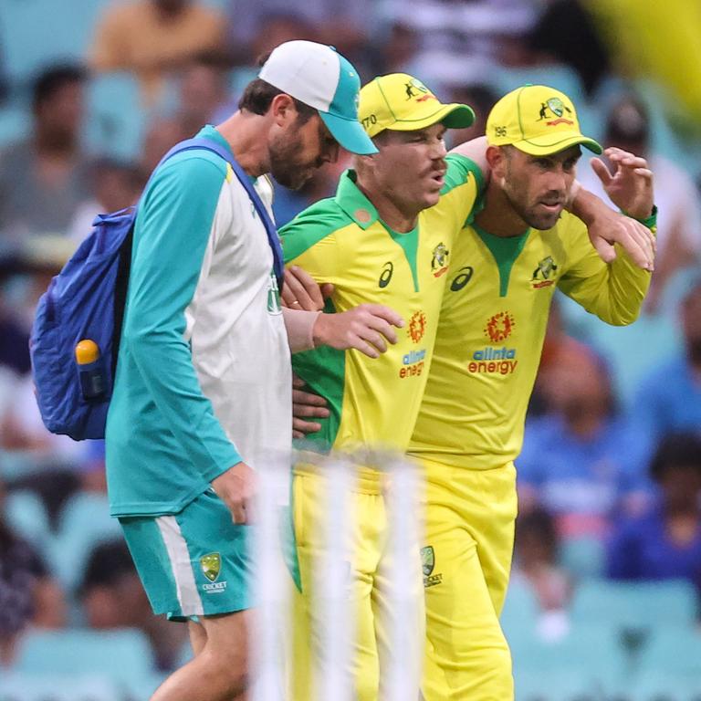 David Warner (C) is assisted by teammate Glenn Maxwell (R) and a trainer as he leaves the field after he suffered a groin injury during the one-day cricket match against India at the Sydney Cricket Ground. Picture: David Gray/AFP