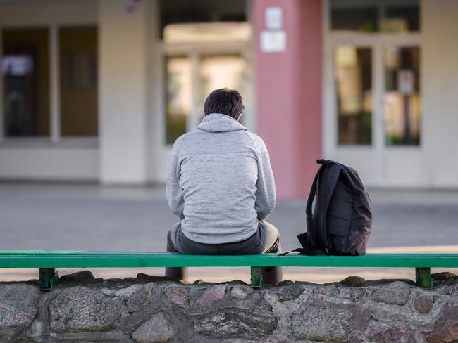 One young man sitting on bench at school yard. Break time. Back view.  - picture istock