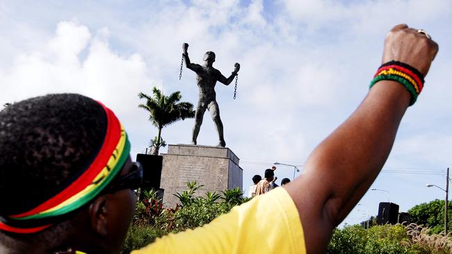 A Barbadian raises his fist in front of a statue depicting the enslaved African Bussa breaking the chains of bondage. Picture: AP.