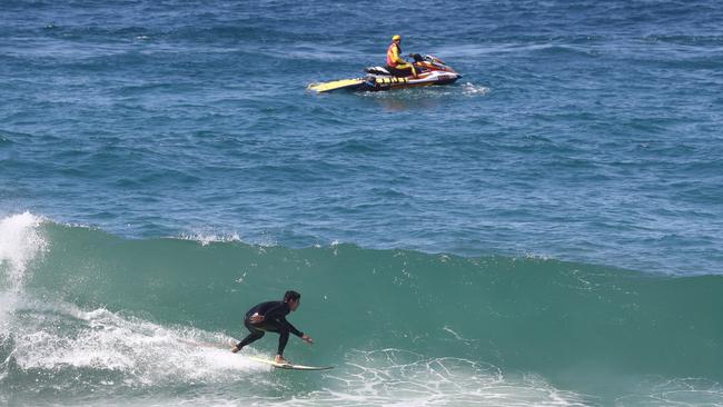 A surfer rides a wave at Burleigh Heads as a Surf Life Saving Queensland lifesaver patrols on a jetski on Sunday. Picture: Jason O'Brien