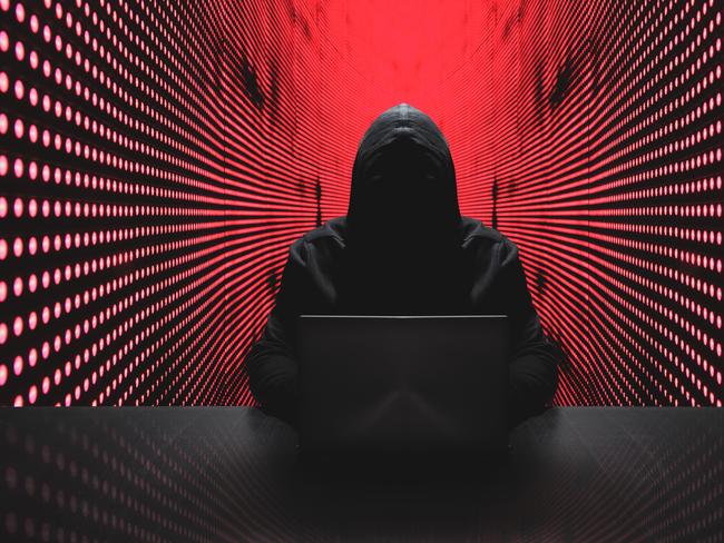 Anonymous hacker in front of his computer with red light wall backgroundAnonymous hacker in a black hoody with laptop in front of a code background with binary streams cyber security concept