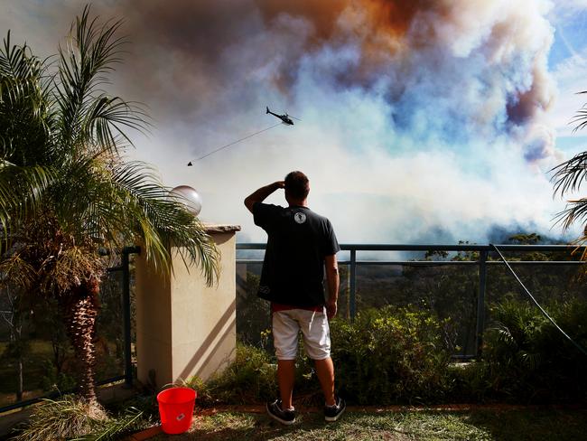 Mark Hopkins watches fire bombing helicopters drop water near his home on Lomandra Place at Alfords Point. Picture: Toby Zerna