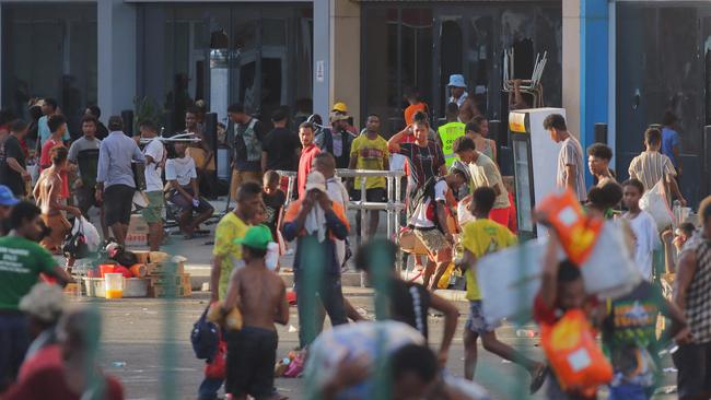 People carry items as crowds leave shops with looted goods amid a state of unrest in Port Moresby. Picture: AFP