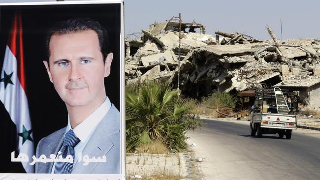 A vehicle drives past a poster of Syrian President Bashar al-Assad and destroyed buildings in a government held neighbourhood of the central Syrian city of Homs. Picture: AFP