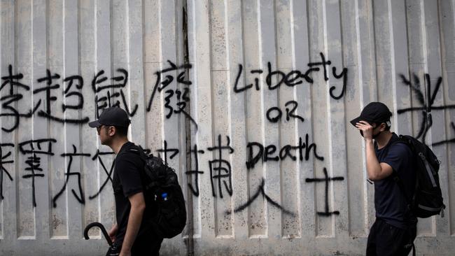 Pro-democracy protesters walk past graffiti during a march in the Hung Hom neighborhood of Hong Kong yesterday. Picture: Getty Images