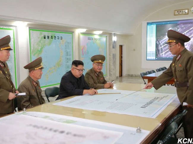 President Kim Jong-un being presented with plans to launch ballistic missiles towards the US territory of Guam. The map in front of him details the flight path of a missile over southern Japan, while the photo on the back wall shows Guam’s Andersen Air Force Base. Picture: KCNA