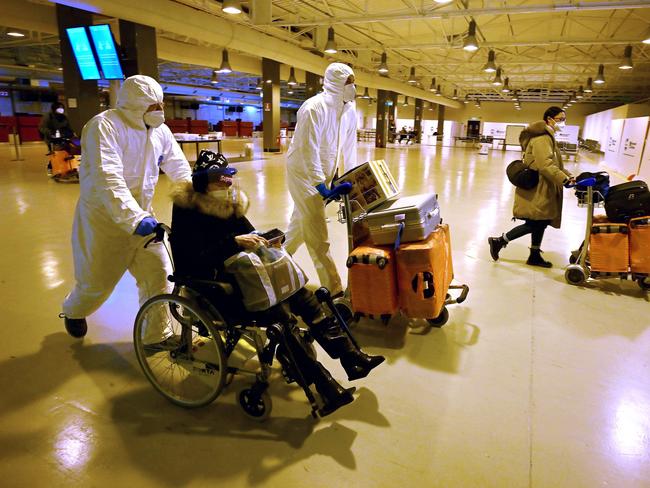 Workers wearing protective masks and suits help Chinese travellers leaving the arrival hall of Rome’s international airport. Picture: AFP