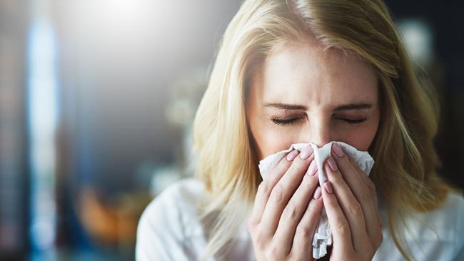 Shot of a frustrated businesswoman using a tissue to sneeze in while being seated in the office