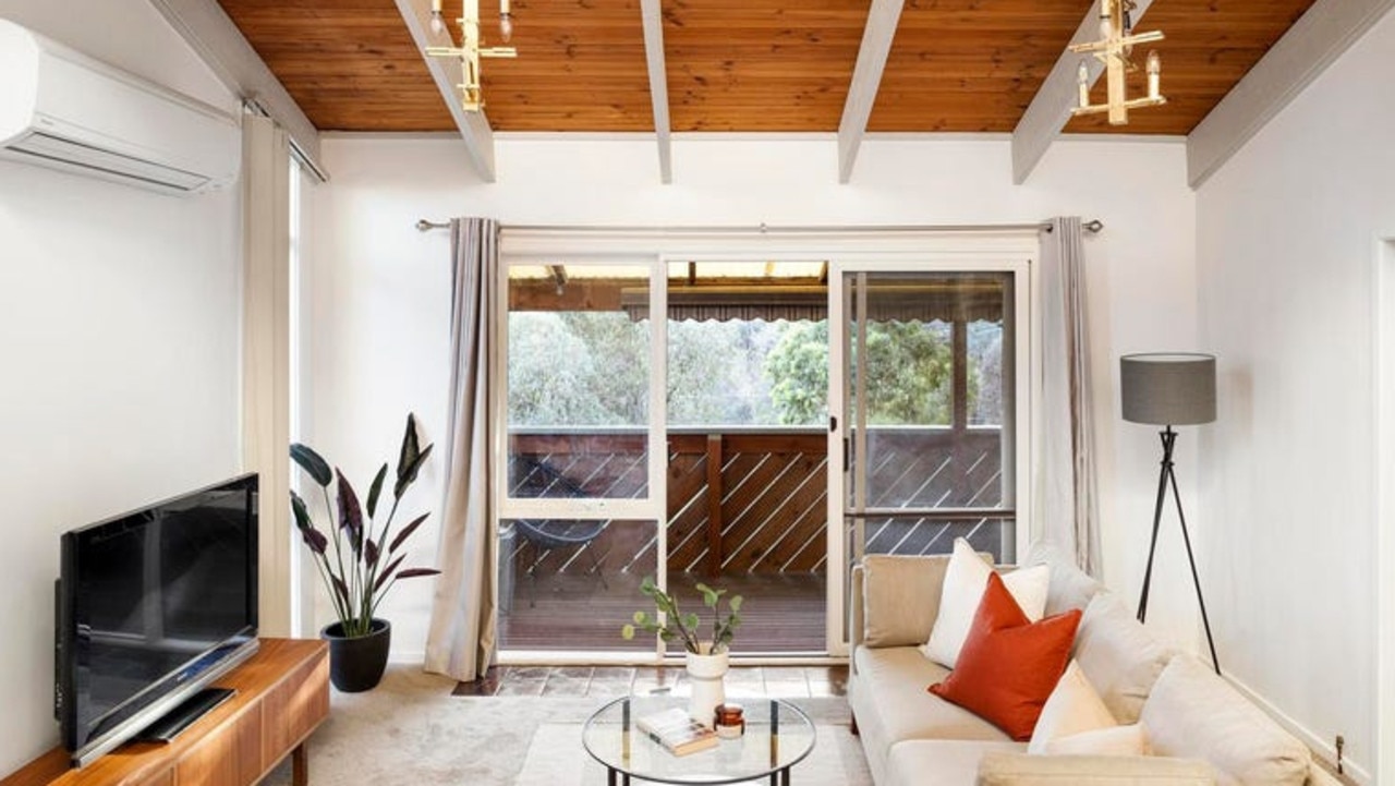 The lounge room, set under a timber-lined cathedral ceiling, extends out to a deck with green views.