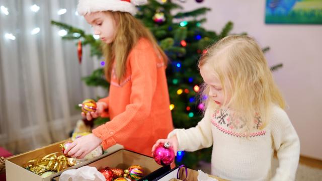 Two adorable little sisters decorating a Christmas tree at home