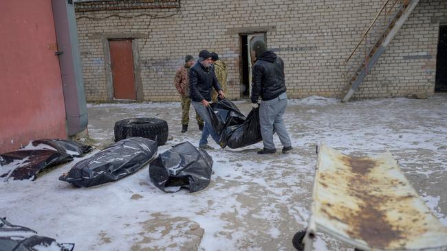 Two men carry a body in a body bag to lay it next to others in a snow covered yard of a morgue in Mykolaiv. Picture: AFP