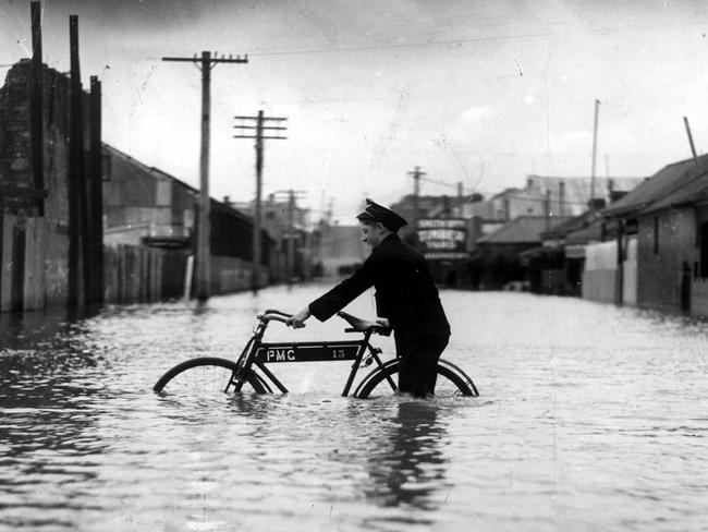 A postman battles to deliver telegrams as floods turn streets by the Yarra River into canals in December 1934. Picture: HWT Library.