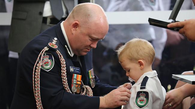 RFS Commissioner Shane Fitzsimmons (L) pins a medal on Harvey Keaton after his father Geoffrey Keaton was posthumously awarded with the Commissioner’s Commendation for Extraordinary Service and a Commendation for Bravery, at his funeral in Sydney. Picture: AFP/RFS