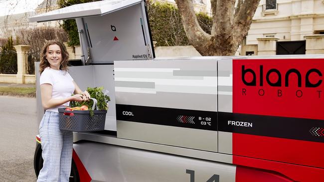 A woman collecting groceries from Applied EV's Blanc Robot.