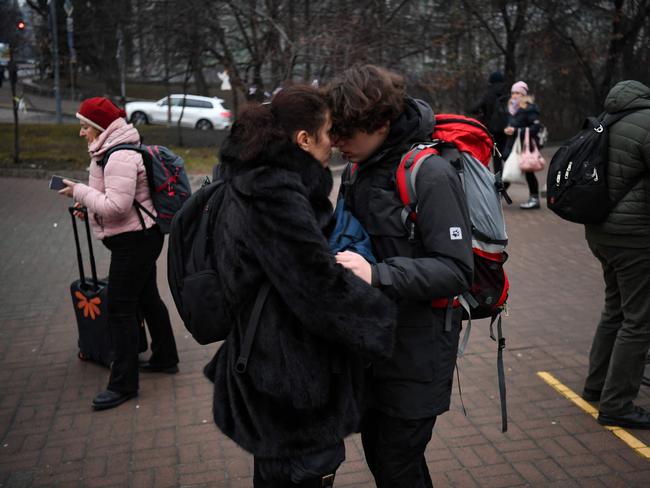 People hug as a woman with a suitcase passes by outside a metro station in Kyiv on the morning of the invasion. Picture: AFP