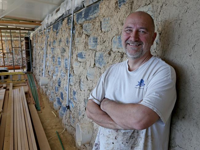 SATURDAY TELEGRAPH - Mark Van Laarhoven is building a house using materials like used car tyres and empty beer bottles on his property near Marulan. When finished the house won't require heating or cooling and will run off solar power. Mark stands in front of a partially rendered wall that has used some of the 1100 car and 4WD tyres that have been used in the construction of the house. Picture: Toby Zerna