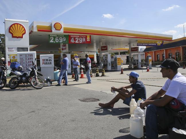 People sit with their containers as they wait at a gas station that is expecting a delivery to refuel, in Sao Paulo, Brazil, Tuesday, May 29, 2018. Brazilian truckers frustrated by rising fuel prices are striking for a ninth day in several states, though sporadic deliveries of gasoline and goods are starting to ease a shutdown that has led to widespread shortages and disturbances. (AP Photo/Andre Penner)