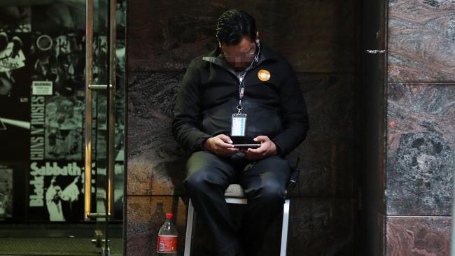 A security guard watching a video on his phone outside the Adina Apartment Hotel near Town Hall. Picture: Jonathan Ng