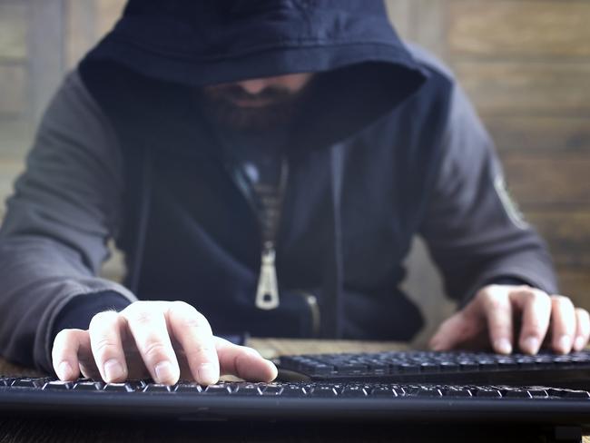 hacker in the black hood in a room with wooden walls makes cybercrime istock image