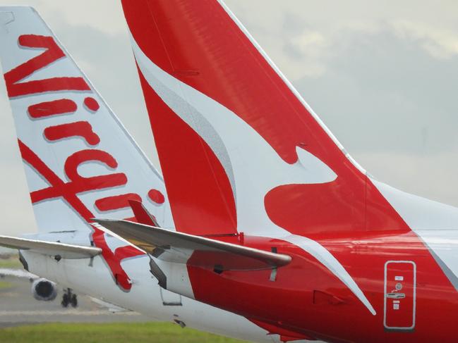 The vertical stabilisers of a Qantas Boeing B737-838 plane, registration VH-VZQ, and a Virgin Australia Boeing B737-8FE plane, registration VH-VUZ, waiting at the northern end of the main runway of Sydney Kingsford-Smith Airport in preparation for departure.  The Qantas plane is heading to Adelaide as flight QF741 and the Virgin plane is heading to Adelaide as flight VA428.  In the background is another Virgin B737-8FE plane. This image was taken from Nigel Love Bridge, Mascot on a sunny afternoon on 3 December 2023.