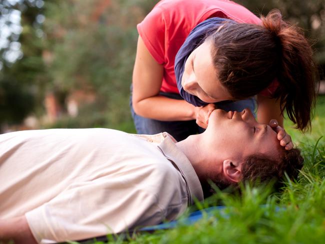 First aid - Look, listen and feel for breathing. Woman is performing first and on a man laying in the grass. She is pulling his head back, listening to his breath and looking at his chest to check if he is breathing. The man is laying unconscious. iStock