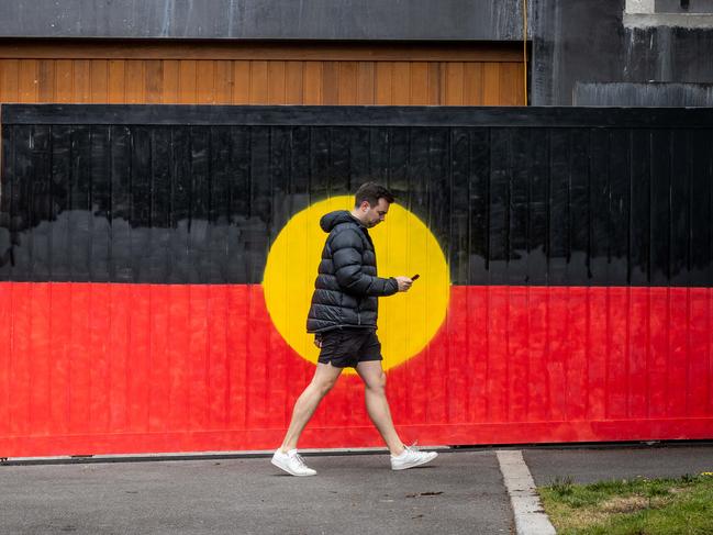 VOICEREF23. A Pedestrian walks past a gate painted in the Aboriginal flag on the day of the referendum in South Yarra, VIC. Melbourne. Picture: Jake Nowakowski