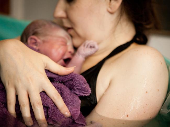 Color photo of a loving mother holding her newborn baby son in the water of a birthing tub immediately after a water birth at home.