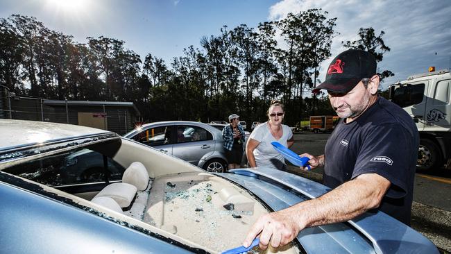 Sherry and Rick Duckworth from Gympie clean the glass out of their car after their back windscreen was shattered during a wild hailstorm at Glenview.  'One minute we were queuing up for fuel eating ice blocks the next we were being absolutely peppered with ice blocks'. Photo Lachie Millard