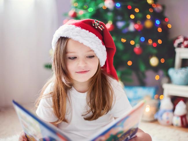 Beautiful girl, reading a book in front of the Christmas tree at home