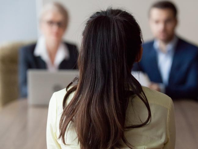 Businesswoman and businessman HR manager interviewing woman. Candidate female sitting her back to camera, focus on her, close up rear view, interviewers on background. Human resources, hiring concept