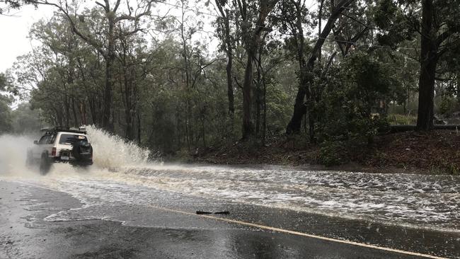 A car drives on the flooded Henry Lawson Drive, East Hills, on Sunday afternoon. Picture: Steve Tuntevski