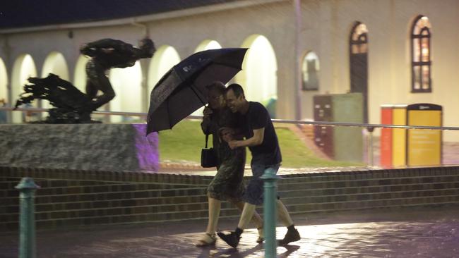 A couple try to protect themselves from the rain at Bondi last night. Picture: Christian Gilles