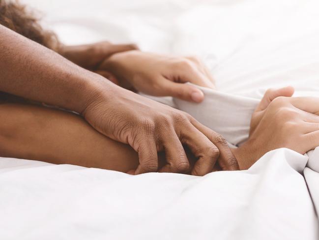 Passion in bed. African-american couple hands pulling white sheets in ecstasy, closeup