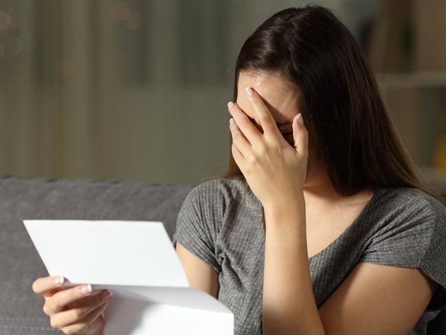 Sad woman reading a letter in the dark at home, renter, tenant, eviction, bill, stress, anxiety - for Herald Sun realestate