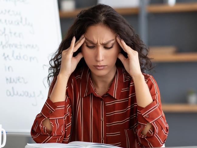 Tired From Work. Portrait of exhausted stressed young woman suffering from headache, touching and massaging her forehead and temples, sitting at desk near whiteboard, thinking about problems