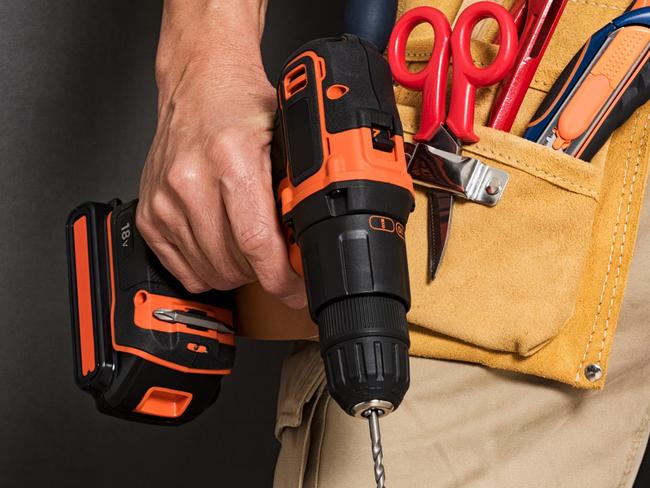 Close up of handyman holding a drill machine with tool belt around waist. Detail of artisan hand holding electric drill with tools isolated over grey background. Closeup hand of bricklayer holding carpentry accessories.